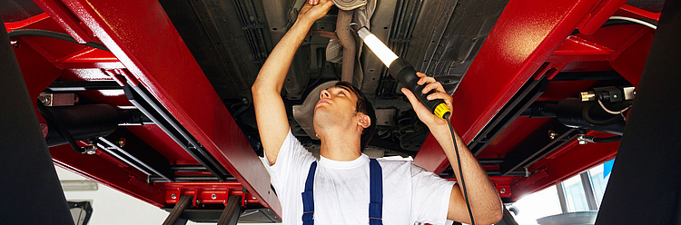 Mechaniker arbeitet unter einem hochgehobenen Auto in einer Autowerkstatt.