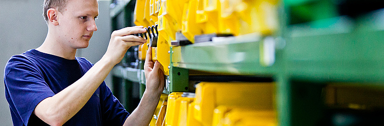 Ein Mechaniker arbeitet fokussiert an der Justierung einer großen gelben Industriemaschine.