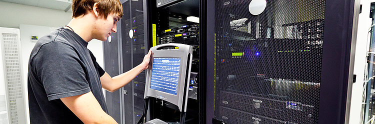 Ein Mann liest Informationen auf einem mobilen Computerterminal neben einem geöffneten Serverrack in einem Datenzentrum.