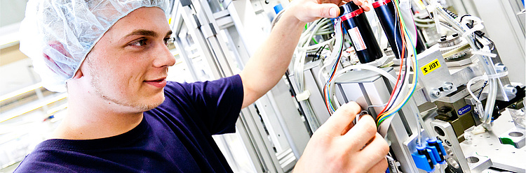 Mann in Schutzkleidung arbeitet an elektrischen Komponenten in einem technischen Labor.