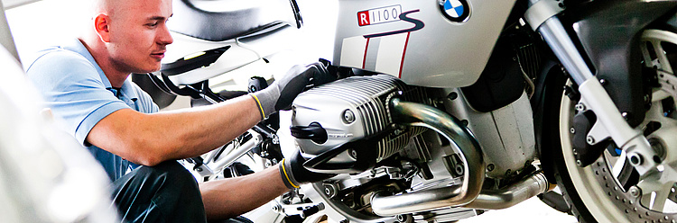 Ein Mechaniker in Arbeitskleidung arbeitet konzentriert an einem BMW-Motorrad in einer Werkstatt.