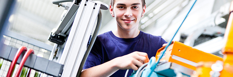 Ein junger Techniker arbeitet lächelnd an einer modernen industriellen Maschine.