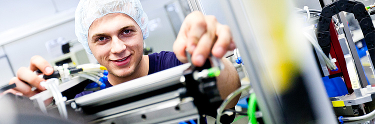 Ein lächelnder Techniker mit Haarnetz arbeitet an einer industriellen Fertigungsanlage.