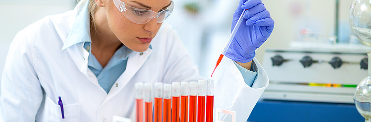 Eine Wissenschaftlerin führt sorgfältig Experimente mit roten Flüssigkeiten in Reagenzgläsern in einem Labor durch.