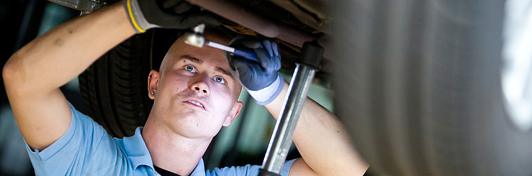 Mechaniker arbeitet konzentriert unter einem aufgehobenen Fahrzeug.