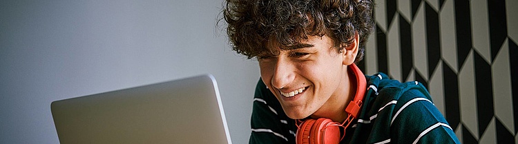 Ein Junge sitzt lachend vor dem Laptop.
