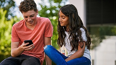 Zwei junge Menschen schauen auf ein Smartphone.