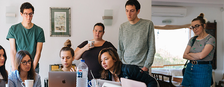 Gruppe von Studierenden arbeitet intensiv zusammen an einem Laptop in einem hellen Raum.