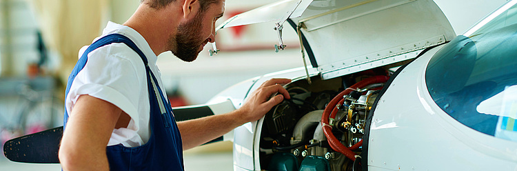 Ein Mechaniker arbeitet an dem Motor eines kleinen Flugzeugs.