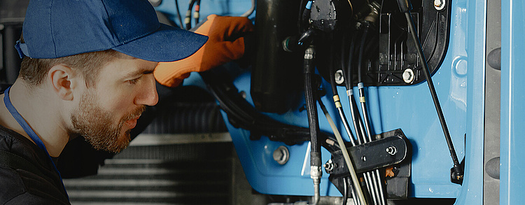 Mechaniker in Arbeitskleidung und Kappe repariert Maschinenkomponenten.