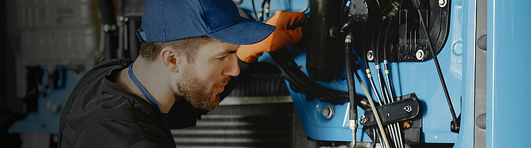 Mechaniker in Arbeitskleidung und Kappe repariert Maschinenkomponenten.