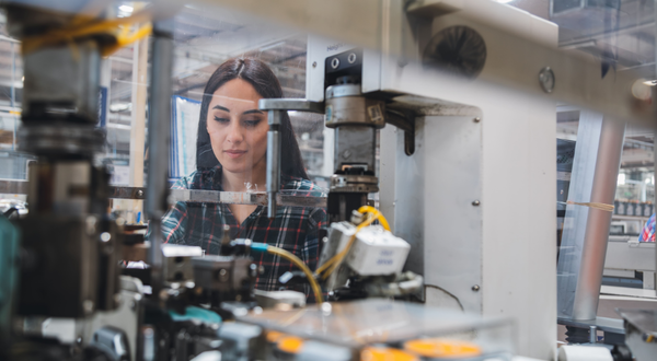 Stanz- und Umformmechanikerin arbeitet konzentriert an einer Maschine mit Metallbauteilen in der Produktionshalle.