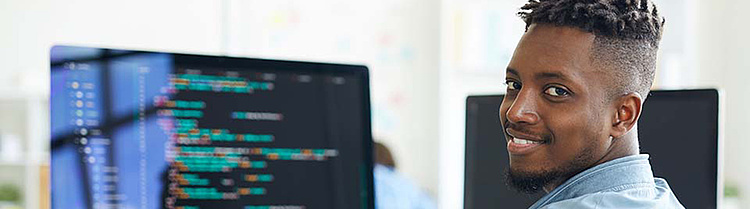 Lächelnder Softwareentwickler arbeitet an Code auf einem Computerbildschirm im Büro.