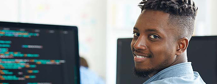 Lächelnder Softwareentwickler arbeitet an Code auf einem Computerbildschirm im Büro.