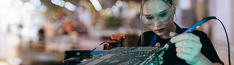 Junge Frau lötet konzentriert an einer Platine während ihrer technischen Ausbildung.