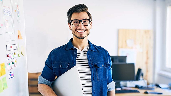 Ein Auszubildender steht mit Laptop unter dem Arm im Büro