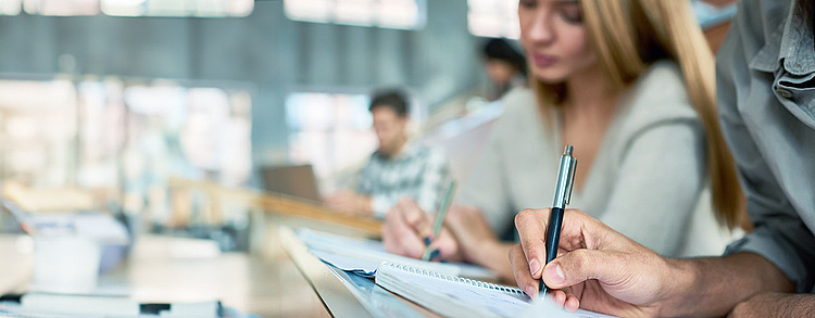 Studierende sitzen in einem modernen Hörsaal und machen Notizen in ihre Hefte. 