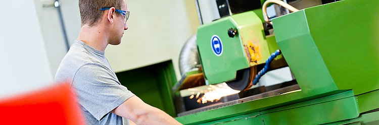 Ein Mann in einer Werkstatt arbeitet an einer grünen Maschine, die bei der Bearbeitung