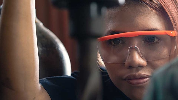 Eine Frau mit Schutzbrille arbeitet handwerklich an einem Projekt