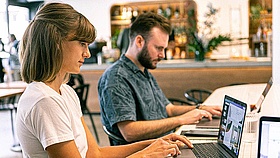 Zwei Menschen sitzen arbeitend vor ihren Laptops.