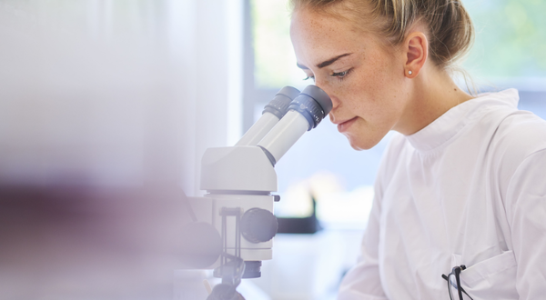 Chemikantin blickt konzentriert durch ein Mikroskop im Labor.