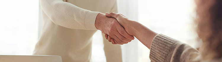 zwei Menschen, die sich die Hände schütteln und einen formellen oder freundlichen Händedruck austauschen. Es symbolisiert Vertrauen, Partnerschaft und Zusammenarbeit.