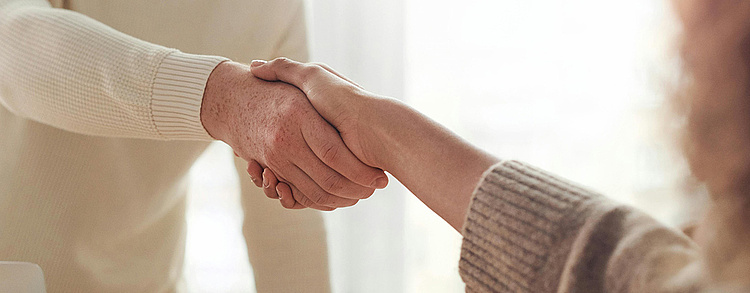 zwei Menschen, die sich die Hände schütteln und einen formellen oder freundlichen Händedruck austauschen. Es symbolisiert Vertrauen, Partnerschaft und Zusammenarbeit.