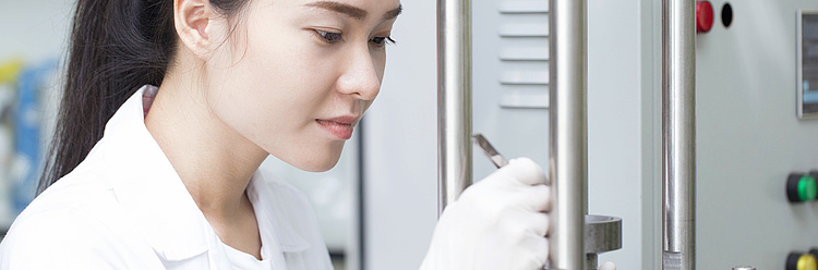 Eine junge Frau im Labor führt eine Messung oder Justierung an einem wissenschaftlichen Gerät durch.