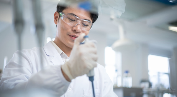 Chemikant mit Schutzbrille und Handschuhen dosiert im Labor konzentriert eine Flüssigkeit mit einer Pipette.