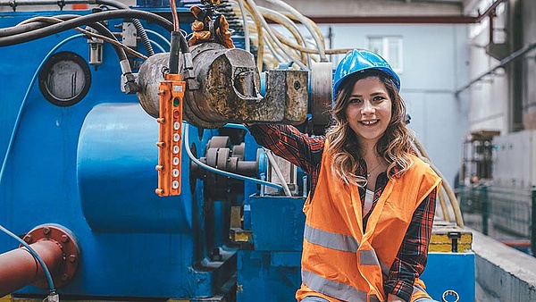 Eine Frau mit Warnweste und Schutzhelm bedient eine Produktionsanlage